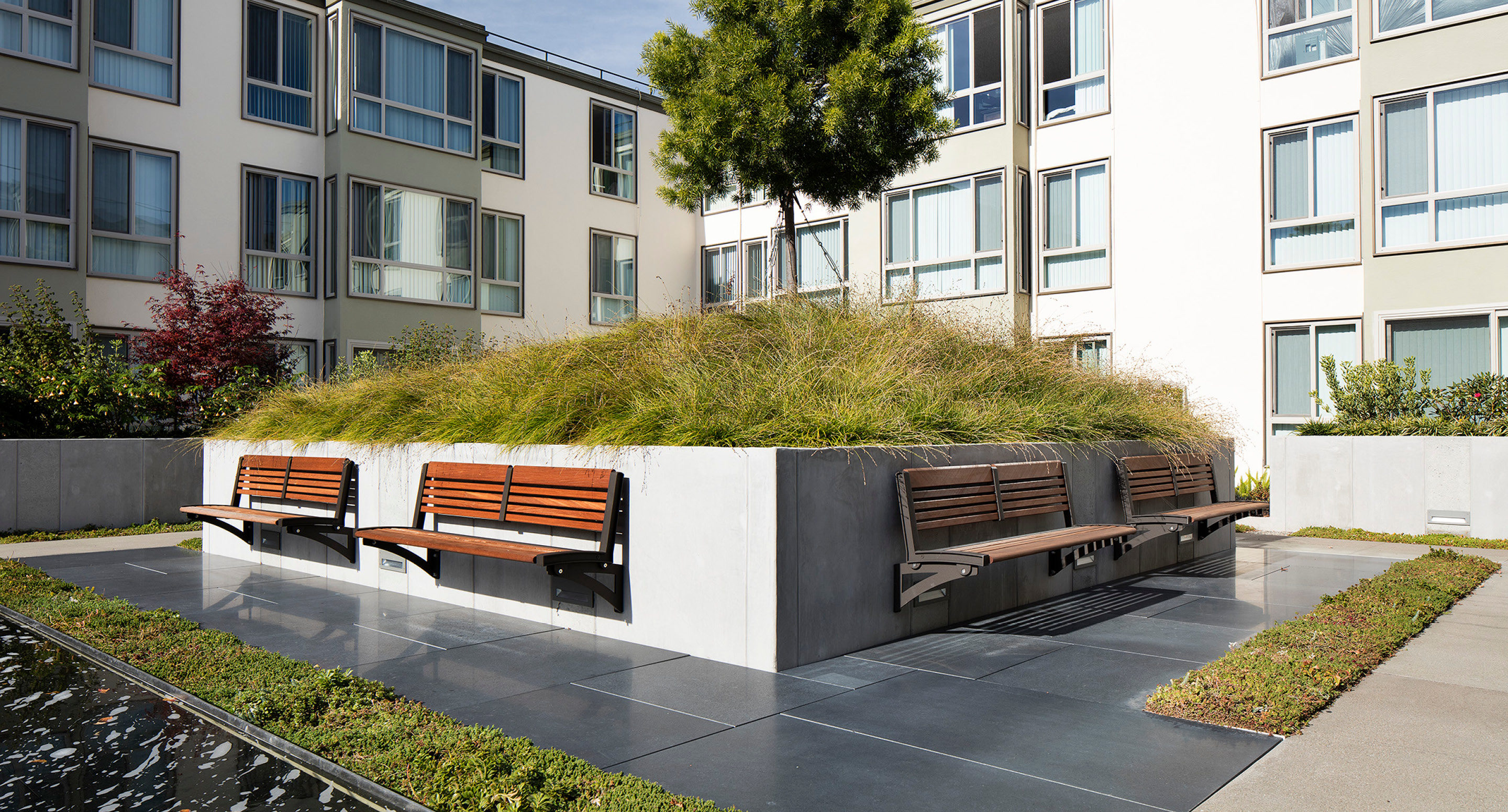 Wall-mount benches attached to large concrete planter within apartment complex