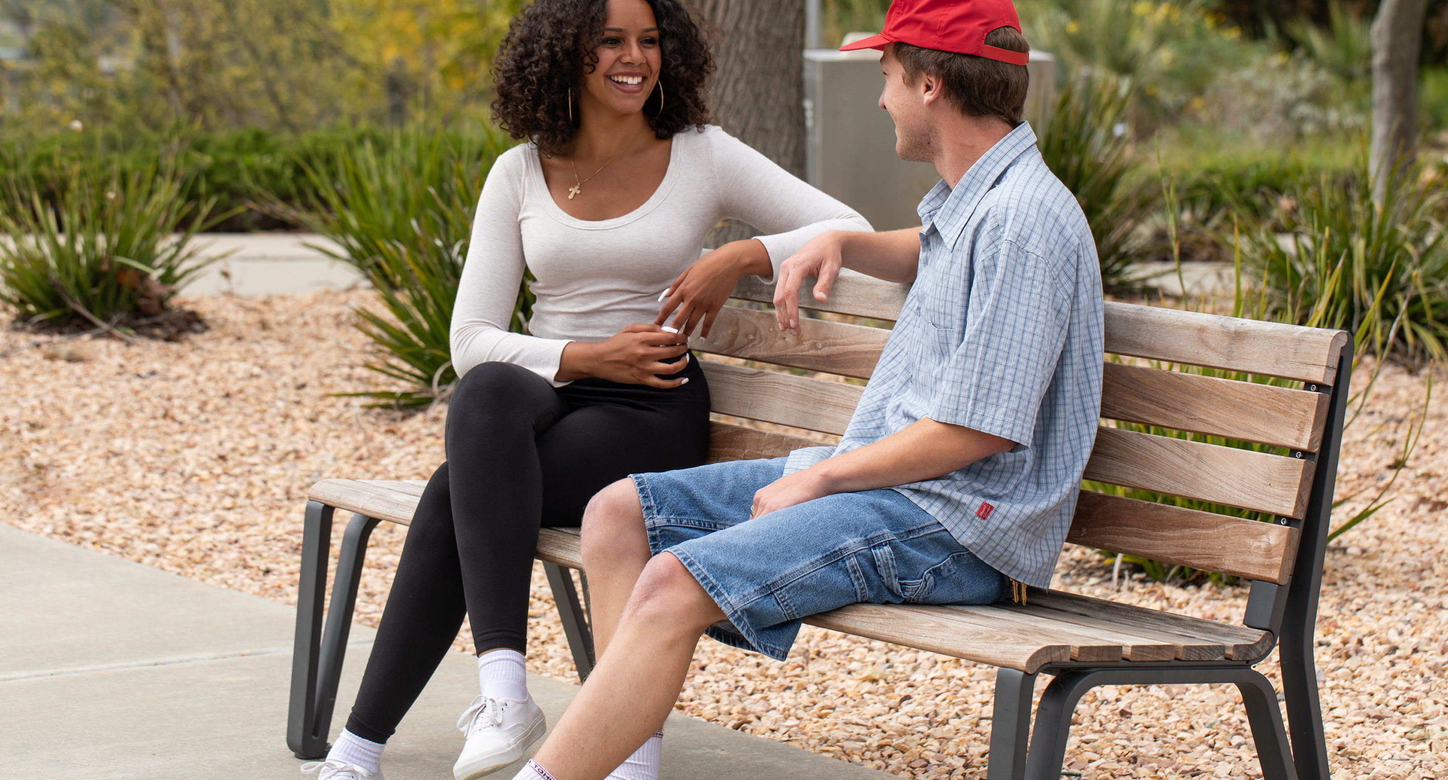 Man and woman sitting on backed wooden bench with stones and greenery in background